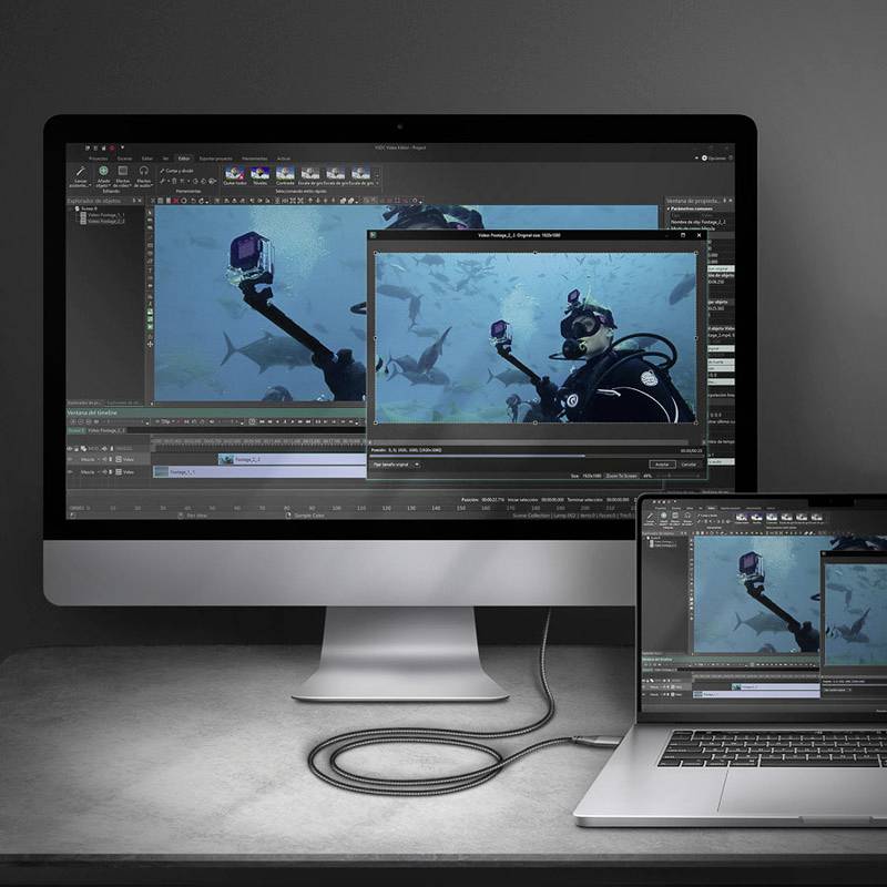 Un écran d'ordinateur et un ordinateur portable affichent une image sous-marine montrant une personne en plongée et des requins. Les deux appareils sont disposés sur une table.