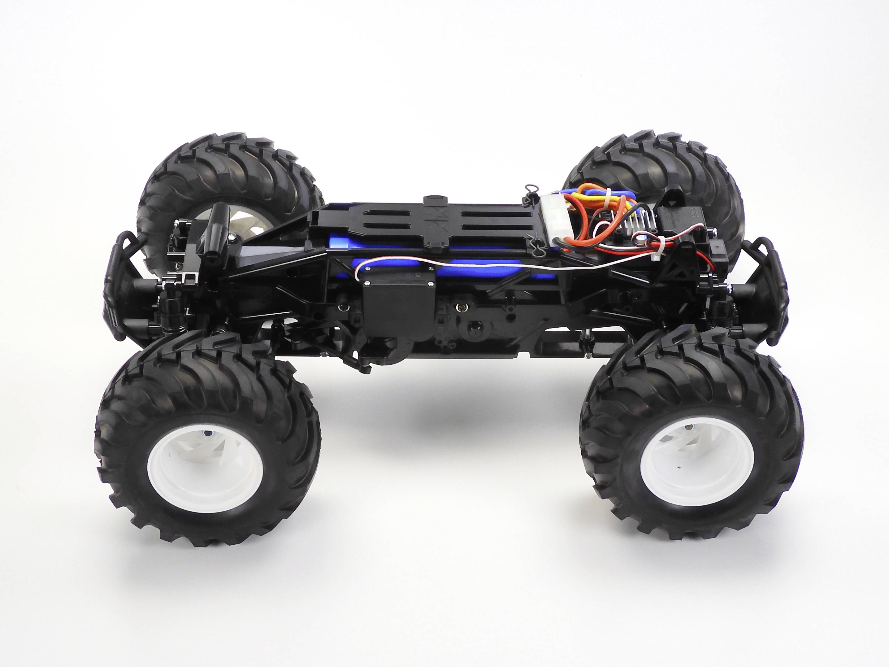 Une voiture miniature noire à quatre roues sans carrosserie. Les grands pneus et l'électronique sur le châssis sont visibles.