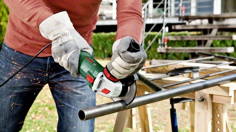 Une personne utilise une meuleuse d'angle pour couper un tuyau métallique. Des étincelles volent de la zone de coupe.