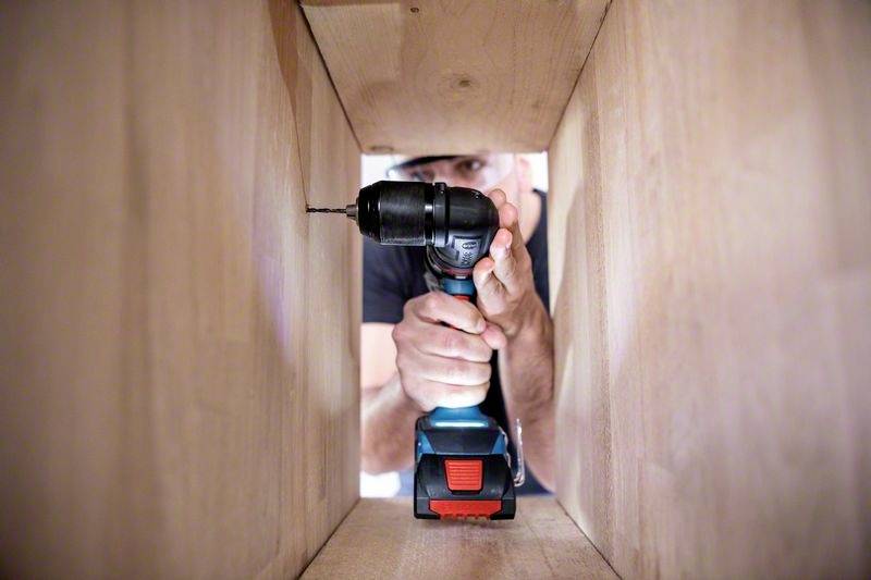 Une personne fore un trou dans une planche de bois à l'aide d'une visseuse-perceuse sans fil.