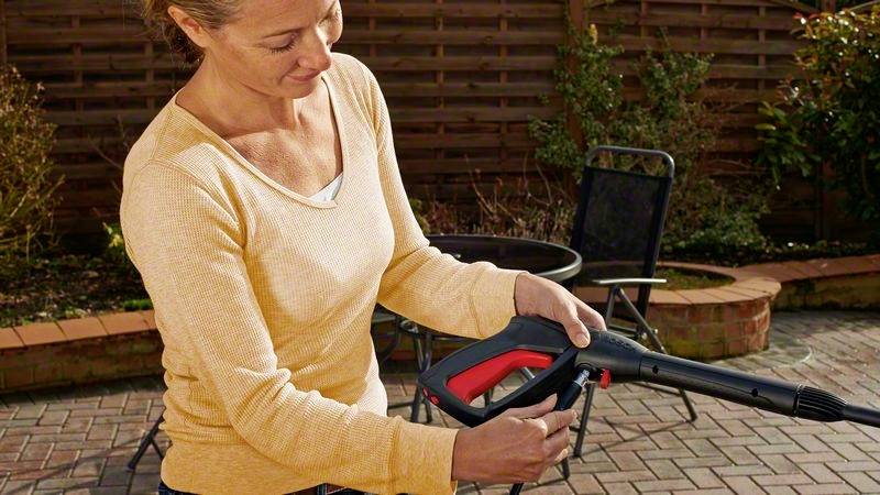 Une personne dans un jardin tient un nettoyeur haute pression. Un table et une clôture sont visibles en arrière-plan.