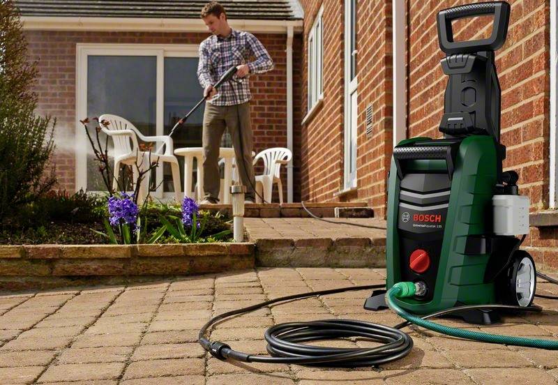 Un homme utilise un nettoyeur haute pression sur une terrasse. Au premier plan se trouve un appareil de nettoyage haute pression Bosch de couleur verte.