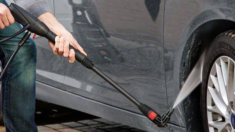 Une personne nettoie le côté d'une voiture avec un nettoyeur haute pression, l'eau giclant contre le véhicule.
