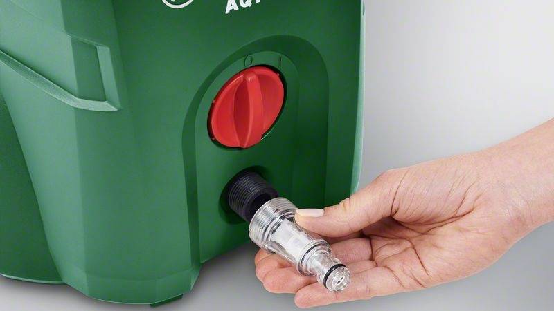 Une main tient une valve transparente devant un appareil vert avec un bouton rouge ; montre la préparation du raccordement.