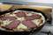 Pizza dans le four avec une couche de fromage et cinq grandes tranches de salami réparties sur la pâte pendant la cuisson.