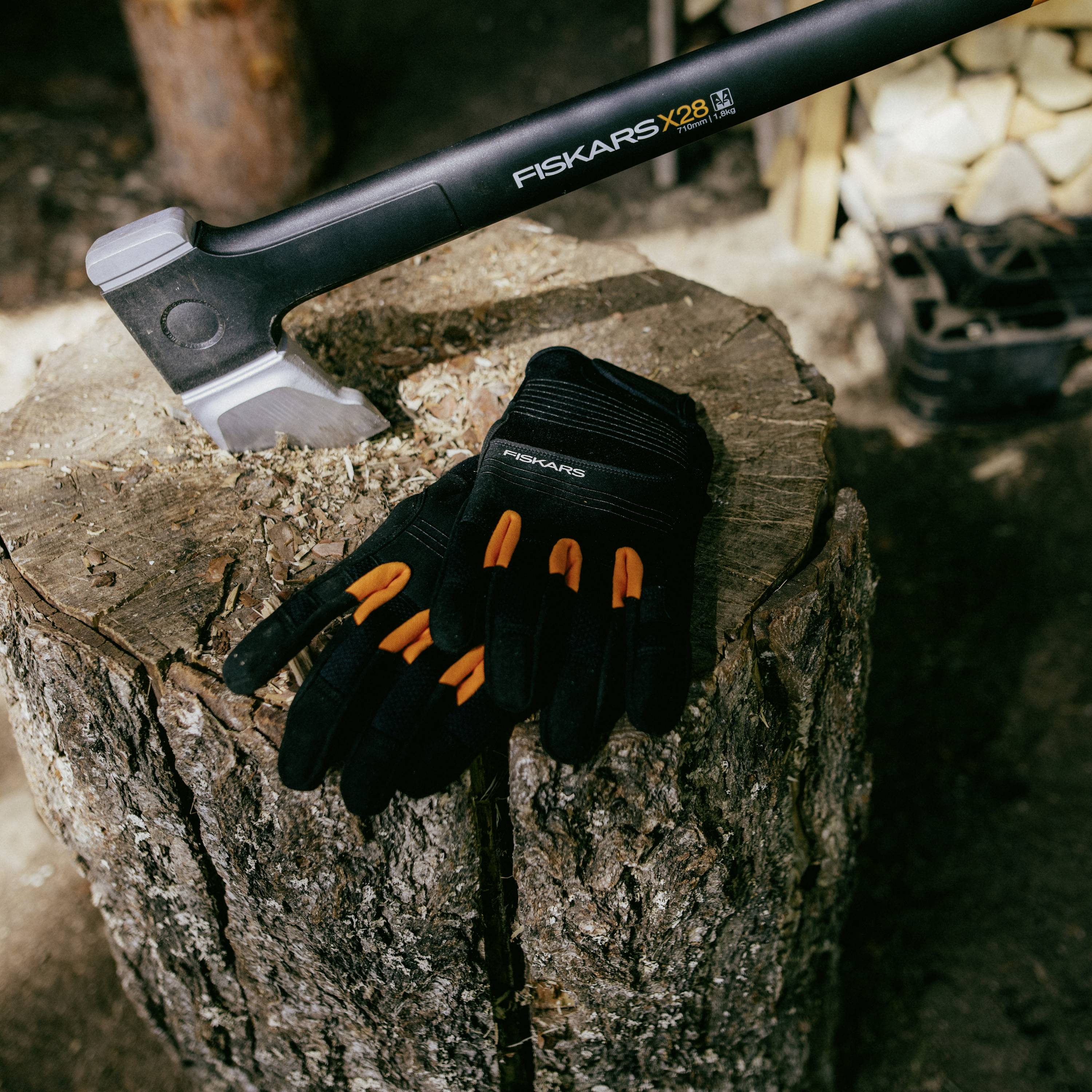La hache est posée sur une souche d'arbre, à côté de gants de travail. L'environnement suggère un lieu de transformation du bois.
