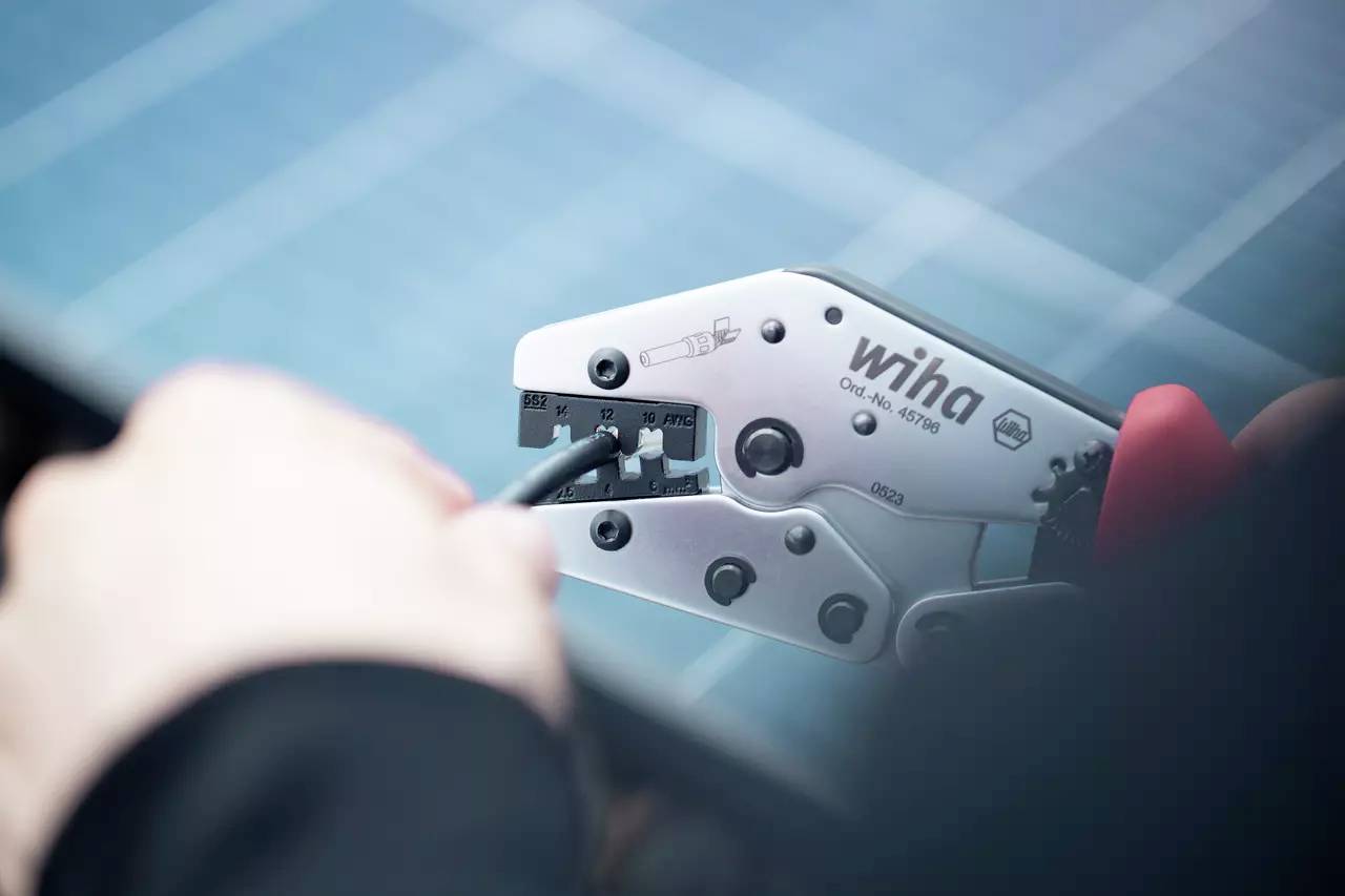 Le gros plan montre une personne qui travaille un câble à l'aide d'une pince à sertir Wiha. La pince enserre fermement le câble.