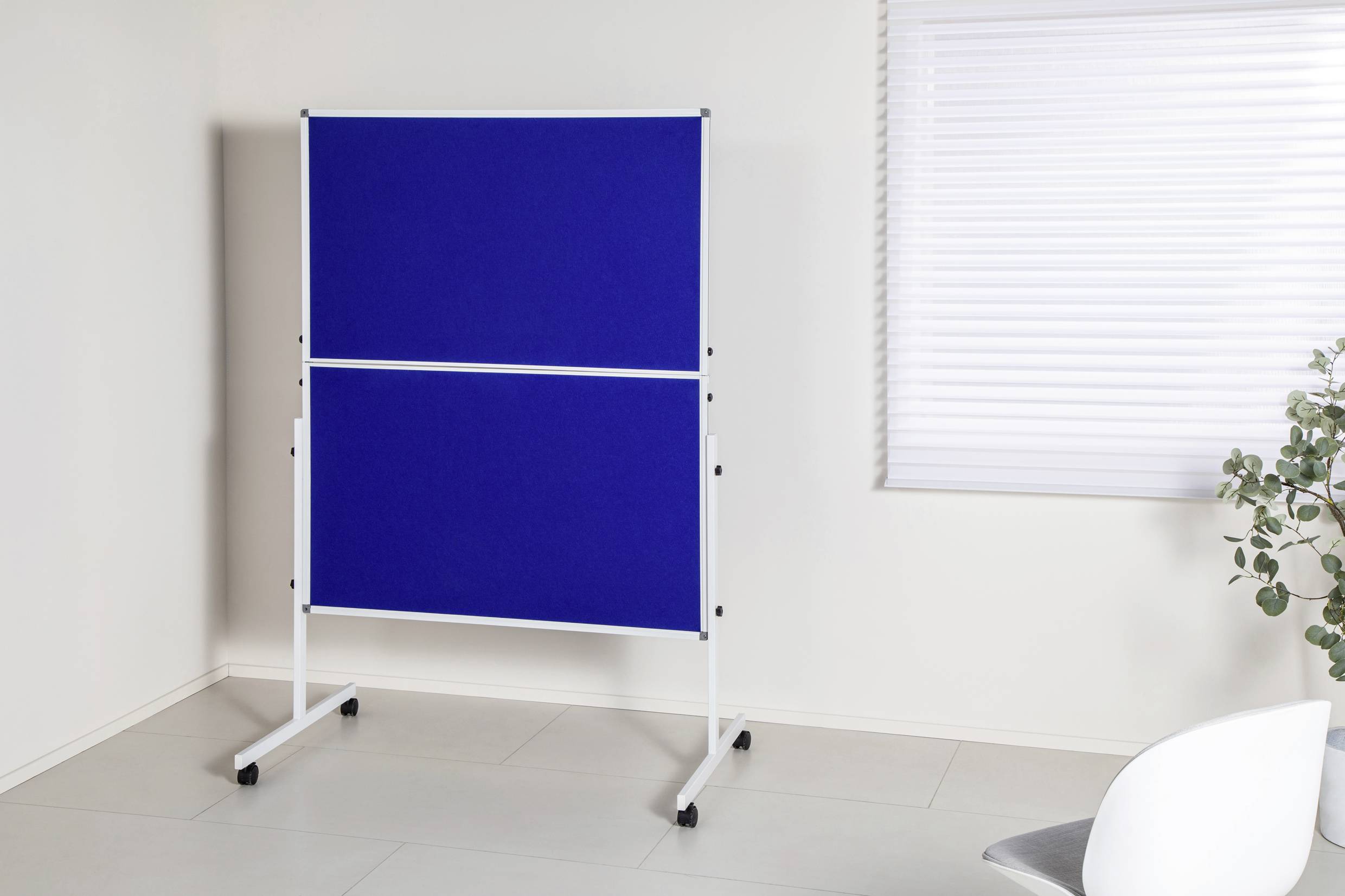 Un tableau blanc bleu sur roulettes est placé dans une pièce lumineuse près d'une fenêtre avec des stores. À gauche au premier plan, on trouve une chaise blanche.