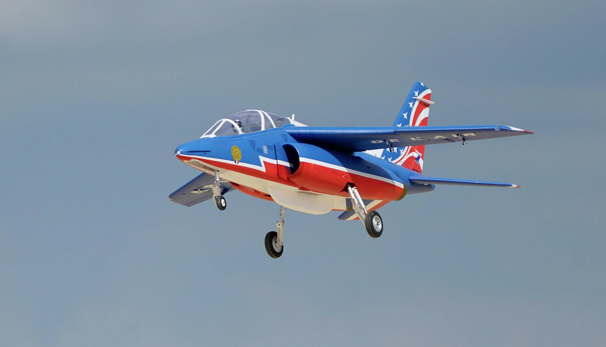 Un petit avion peint coloré avec une peinture bleue, rouge et blanche vole devant un ciel gris-bleu.