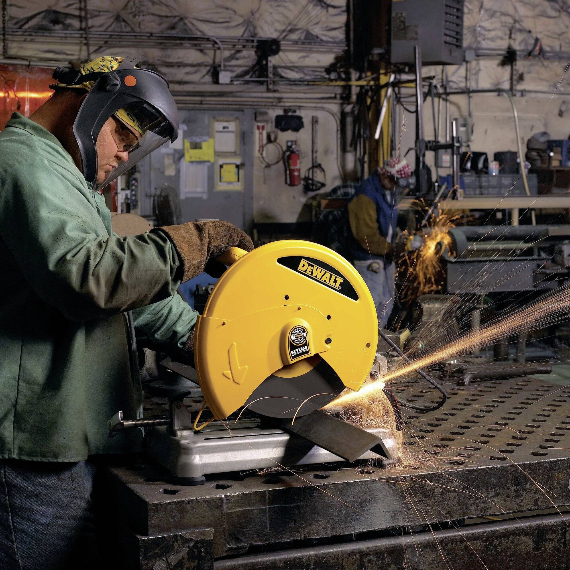 Un ouvrier coupe du métal avec une scie circulaire jaune dans un atelier. Des étincelles volent, des vêtements de protection sont portés.