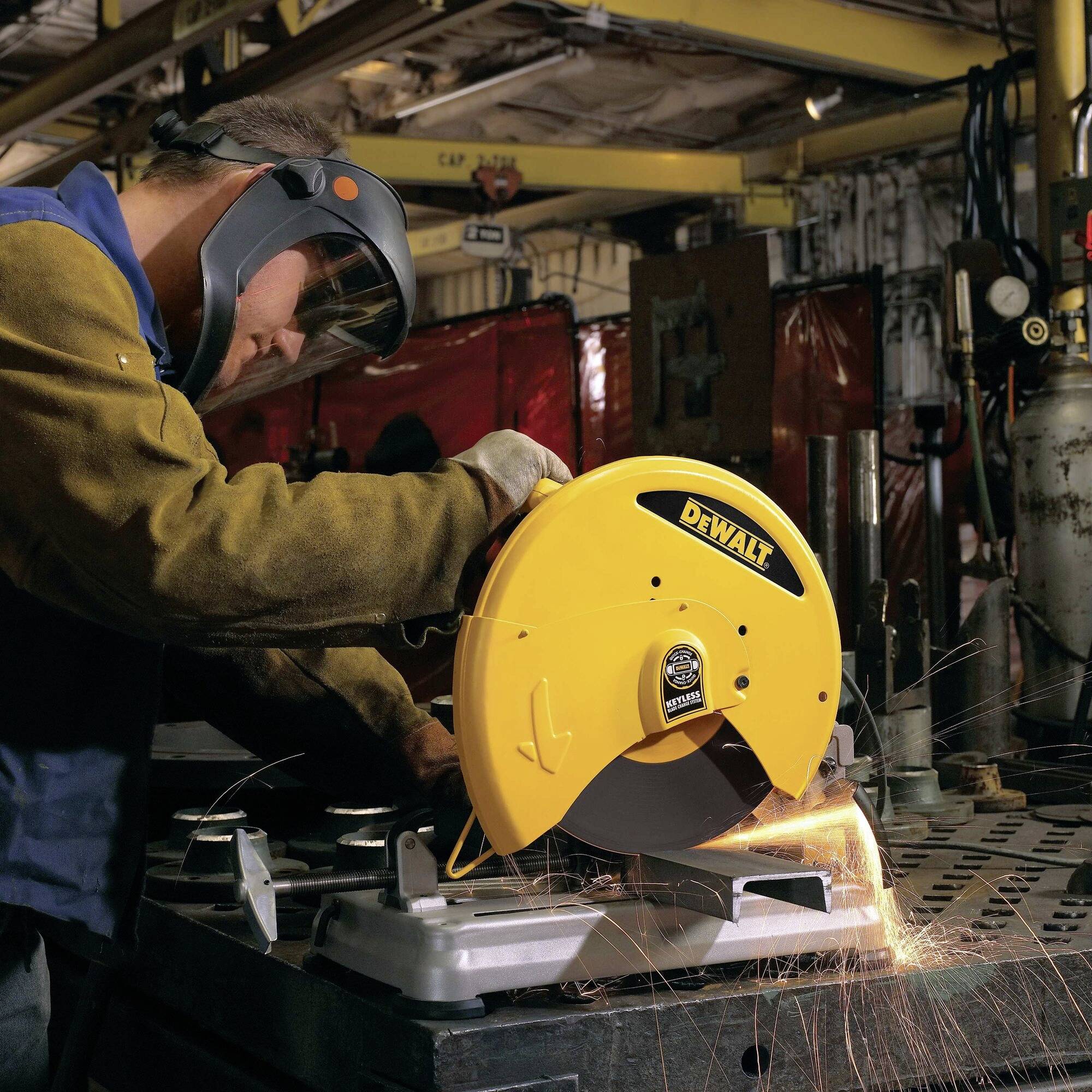 Une personne en tenue de protection coupe du métal avec une scie circulaire jaune dans un atelier, des étincelles volent.