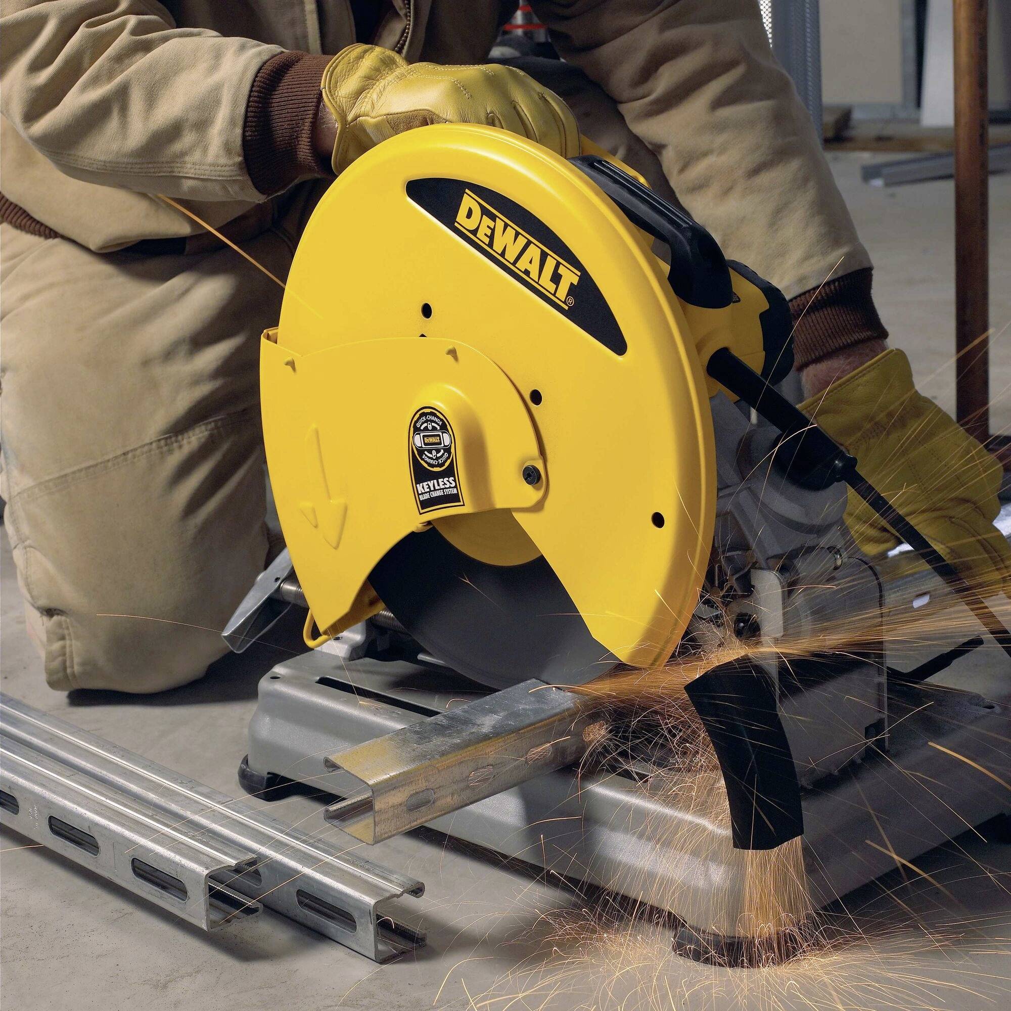 Une personne utilise une scie circulaire jaune pour couper des tuyaux métalliques. Des étincelles jaillissent de la coupe, tandis que la personne porte des gants de travail.