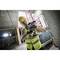 Un ouvrier en gilet de sécurité jaune et casque fore avec une perceuse électrique sur un chantier de construction.
