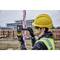 Un ouvrier portant un gilet de sécurité jaune et un casque mesure la hauteur à l'aide d'un appareil électronique fixé sur une perche sur un chantier de construction. Des échafaudages sont visibles en arrière-plan.
