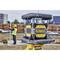 Un nivellement laser jaune de la marque DeWalt sur un chantier de construction, avec un ouvrier en tenue de protection tenant une mire de mesure à l'arrière-plan.