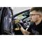 Un homme portant des lunettes de protection utilise un tournevis à batterie jaune pour travailler sur une voiture. L'intérieur de la voiture est visible en arrière-plan.