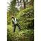 Un jardinier en tenue de protection coupe une haie dans la forêt avec un grand taille-haie.