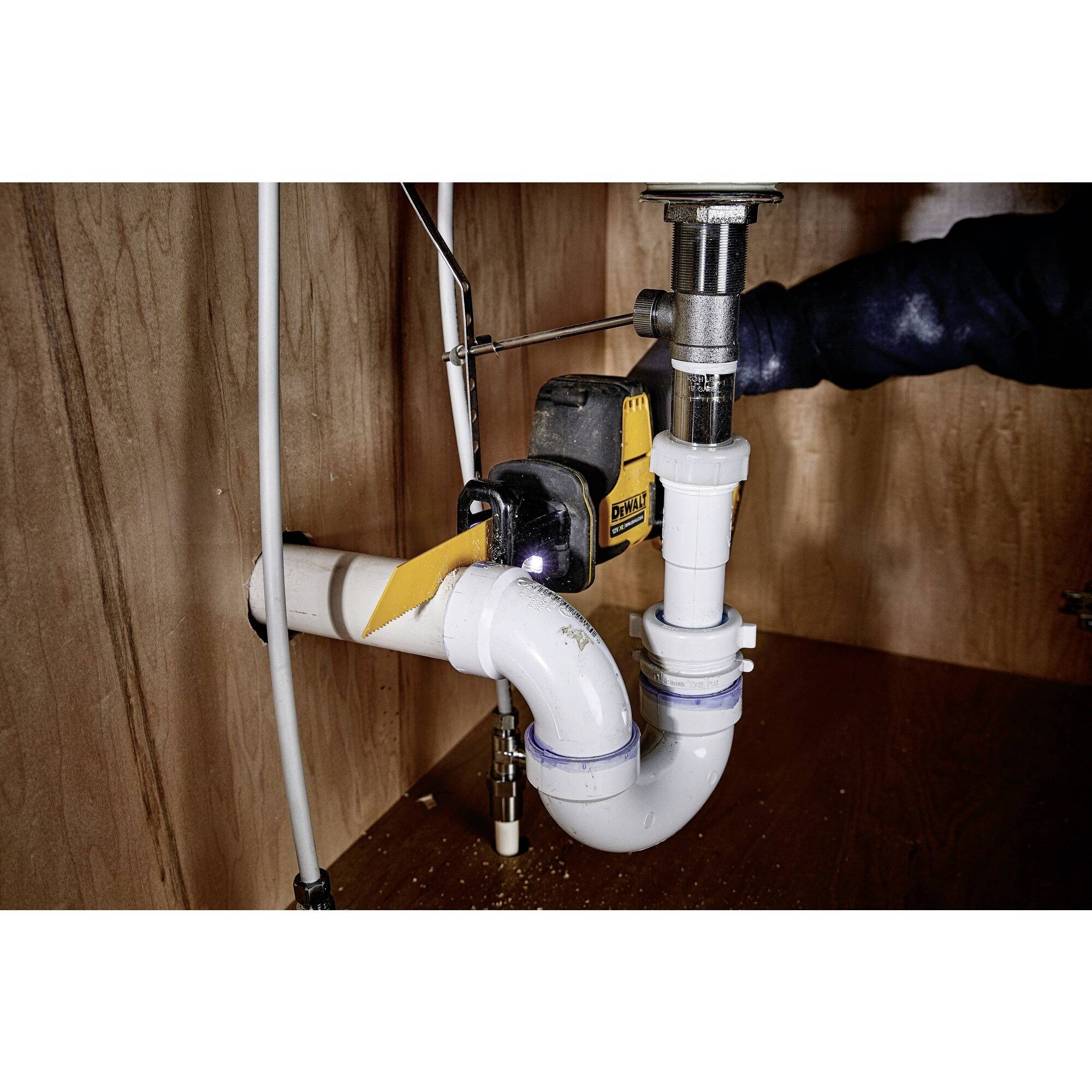 Plombier au travail sous un lavabo, installant un tuyau de vidange en PVC en forme de U, entouré de murs en bois.