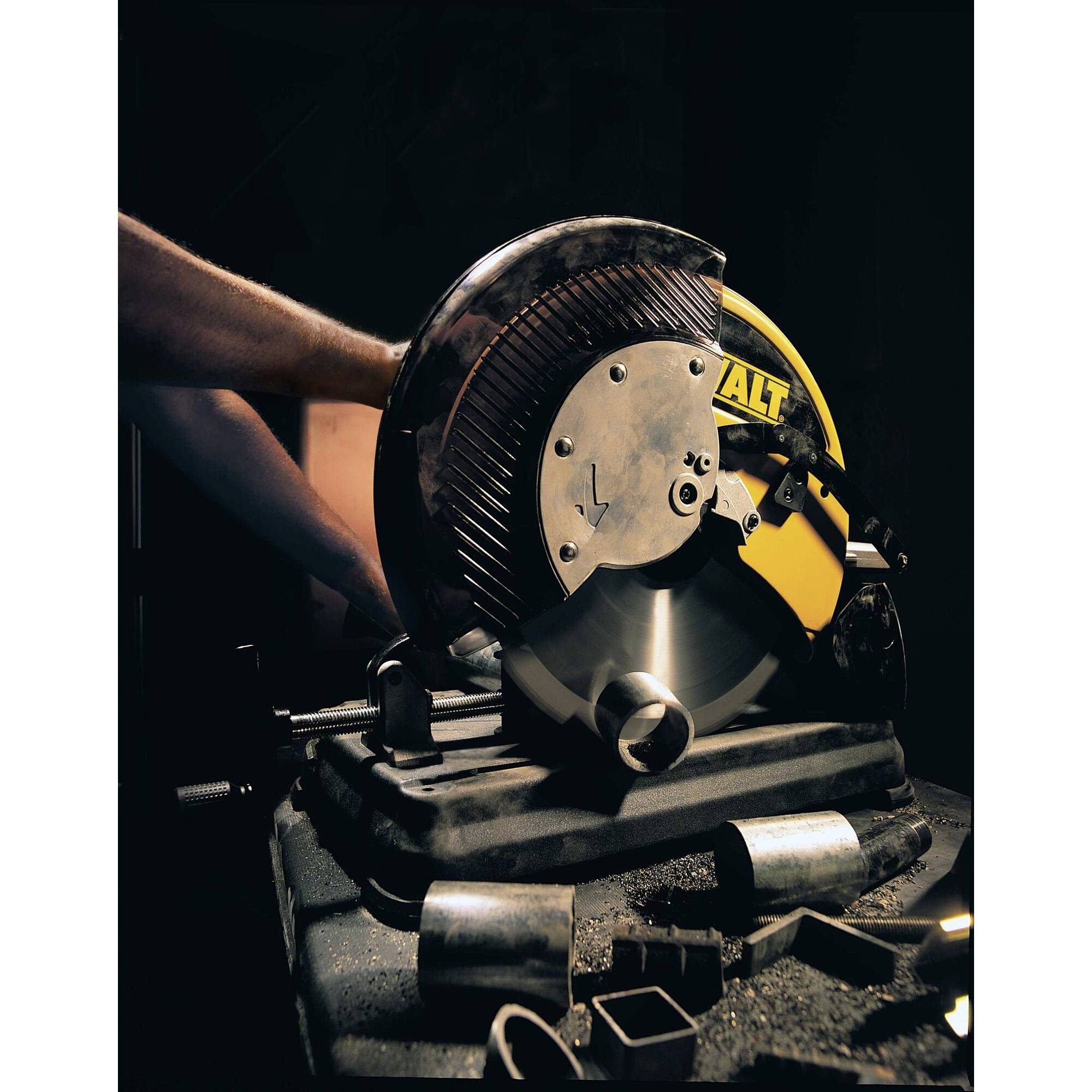 Une personne utilise une scie métallique jaune et coupe un morceau de métal. Des étincelles volent tout autour. À l'arrière-plan, des pièces métalliques sont visibles.