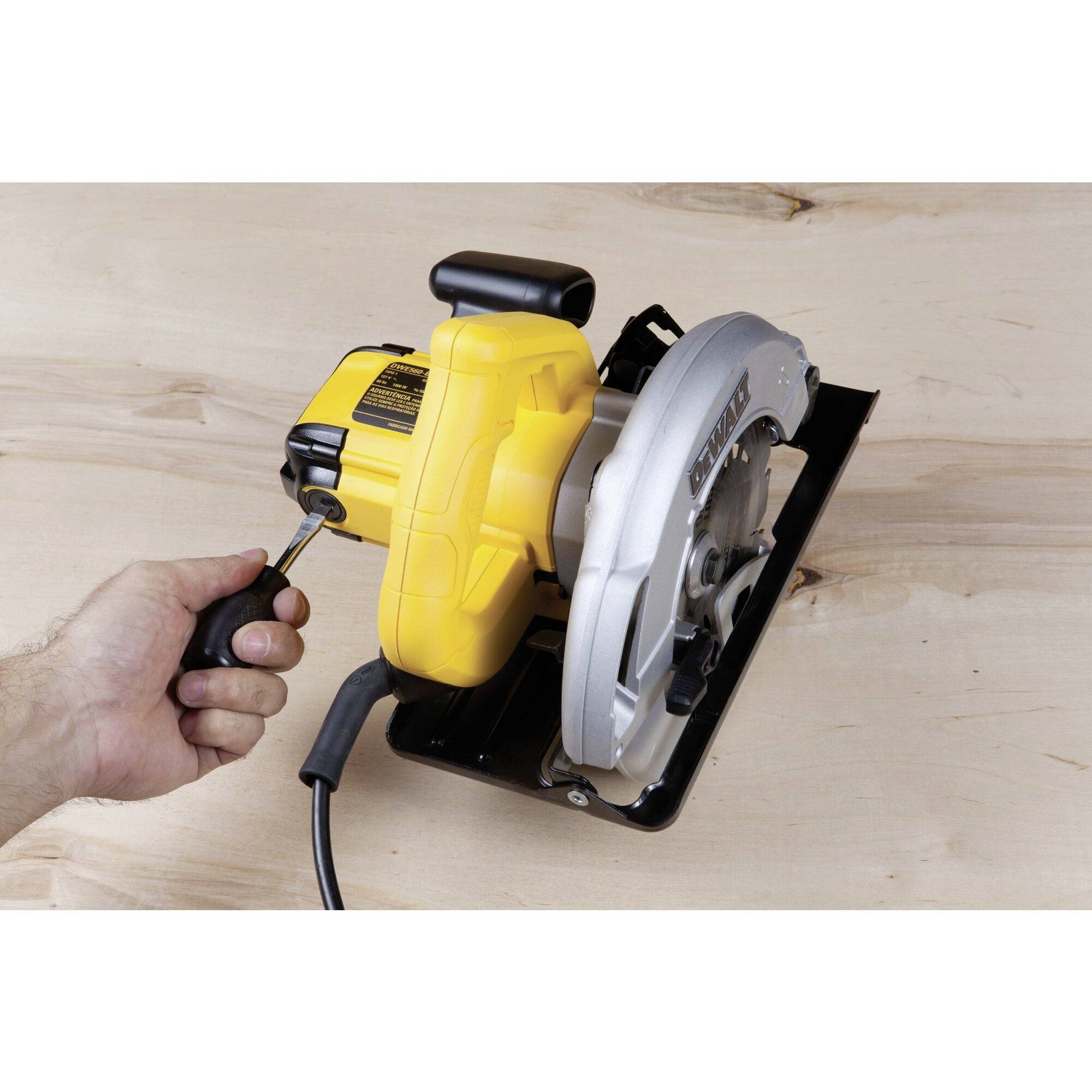 Une main manipule un tournevis pour fixer la lame d'une scie circulaire jaune sur une table en bois.