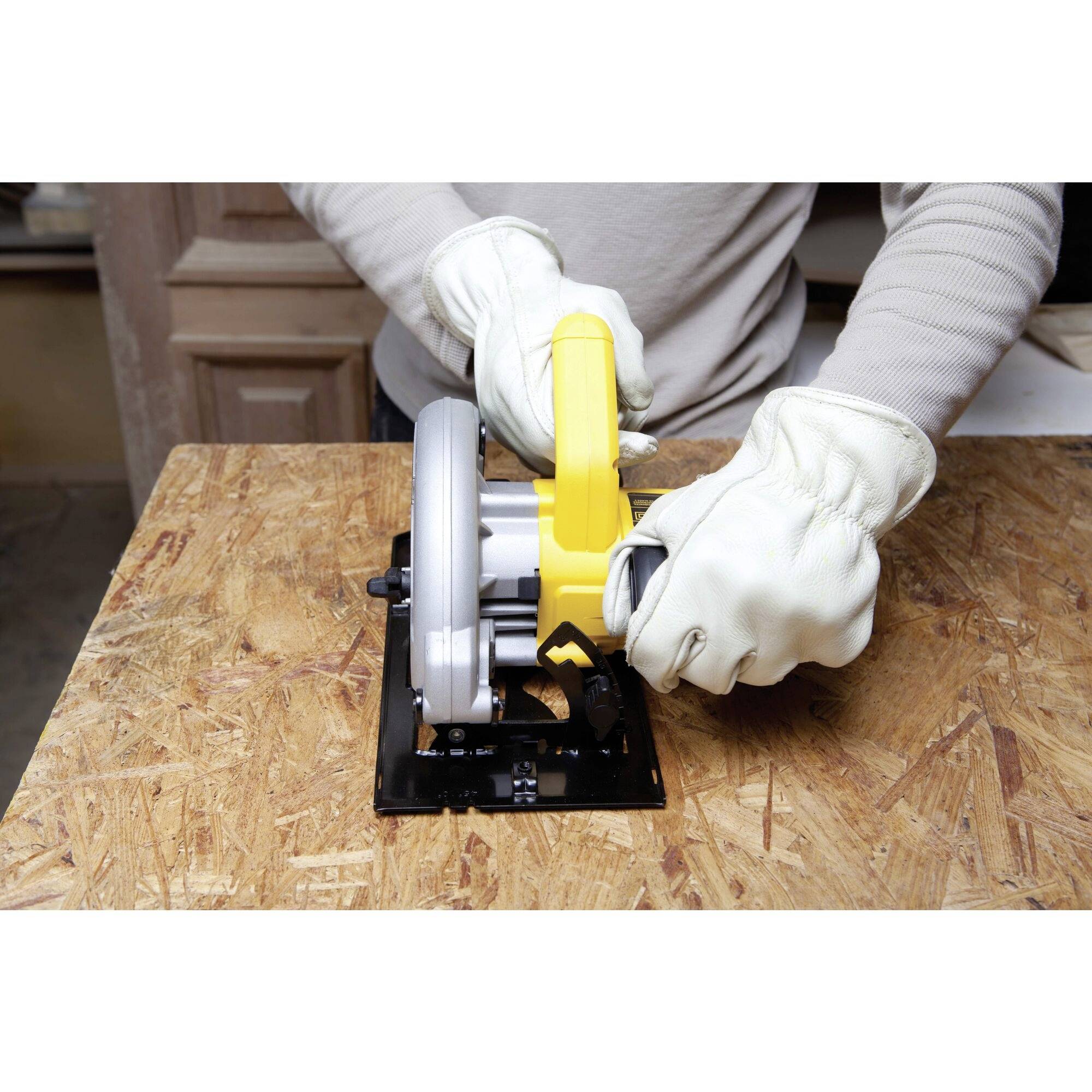 Une personne portant des gants de protection utilise une scie circulaire jaune sur une planche en bois.