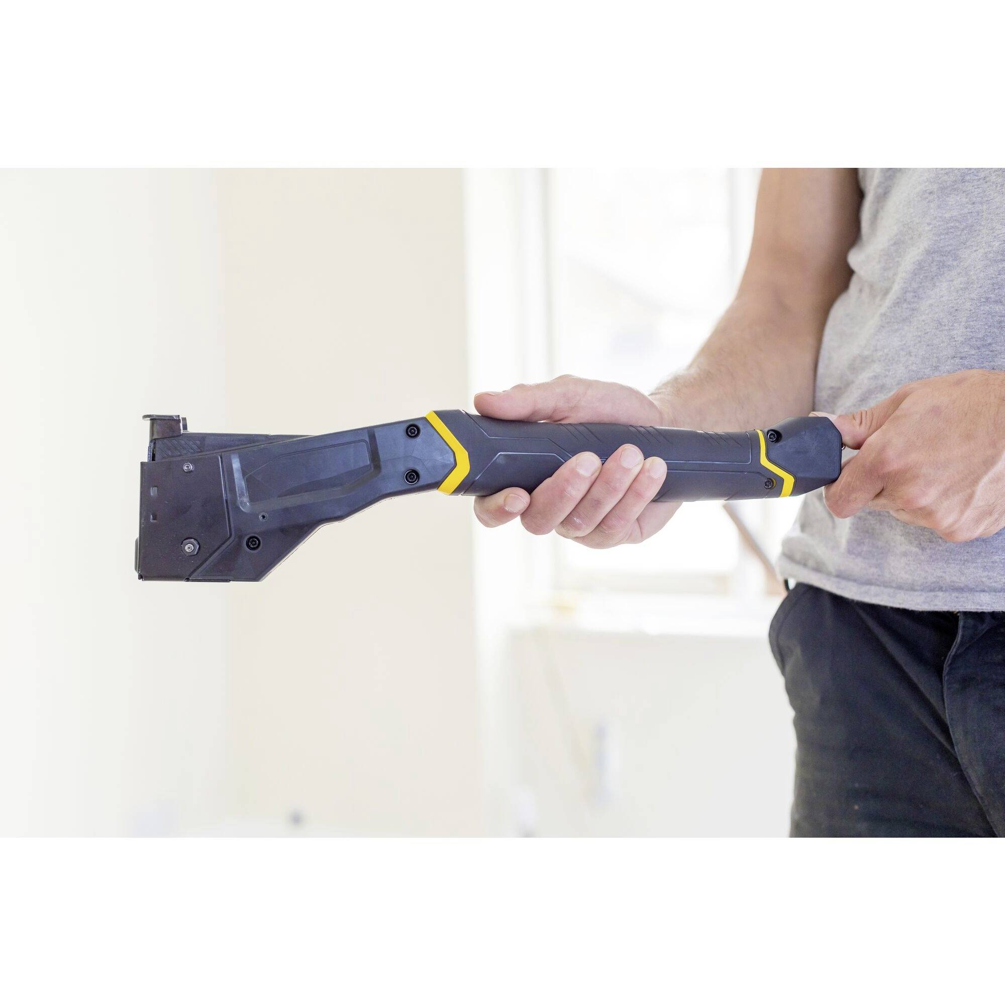 Une personne tient un outil noir avec des détails jaunes dans sa main, probablement adapté à des travaux de construction ou de bricolage.