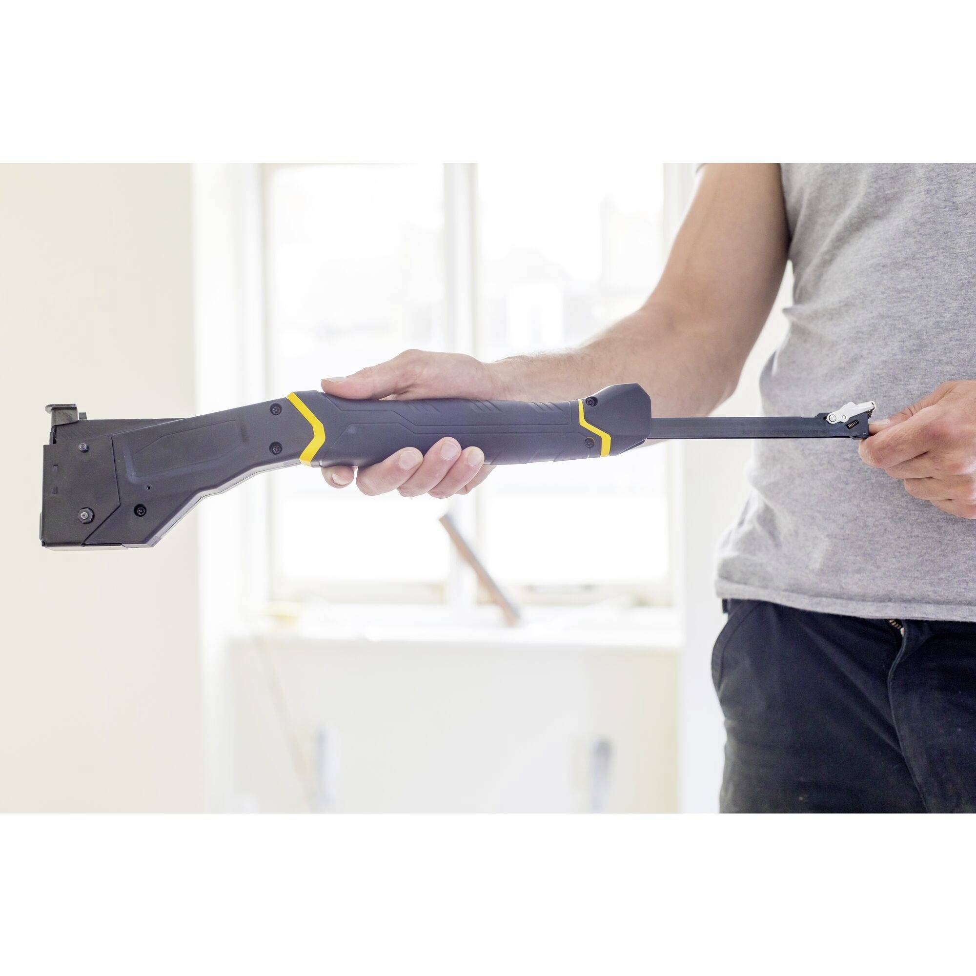 Une personne ajuste un outil noir avec des touches jaunes. En arrière-plan, un chantier de construction.