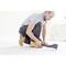 Un homme en tenue de travail utilise un outil de levier pour soulever un tapis. Des murs clairs sont visibles en arrière-plan.