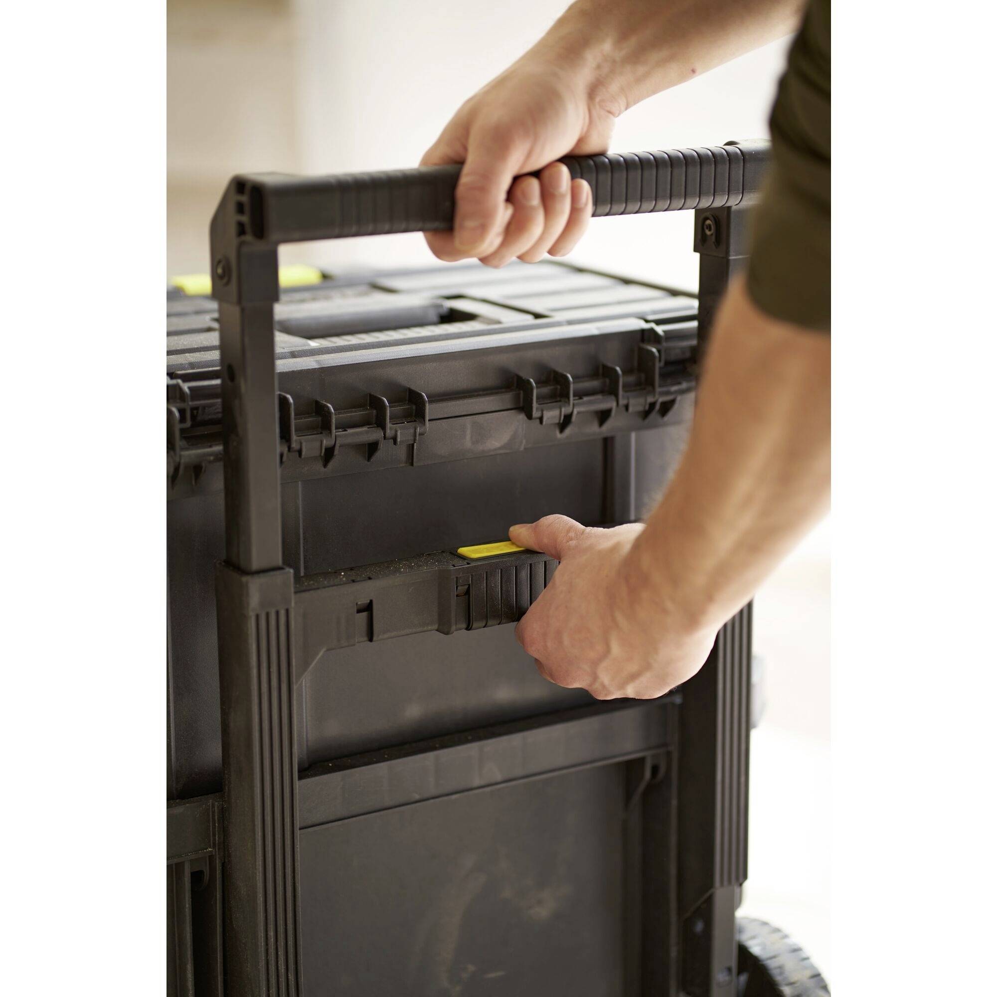 Une personne tire une valise à outils noire sur roulettes avec une poignée télescopique.