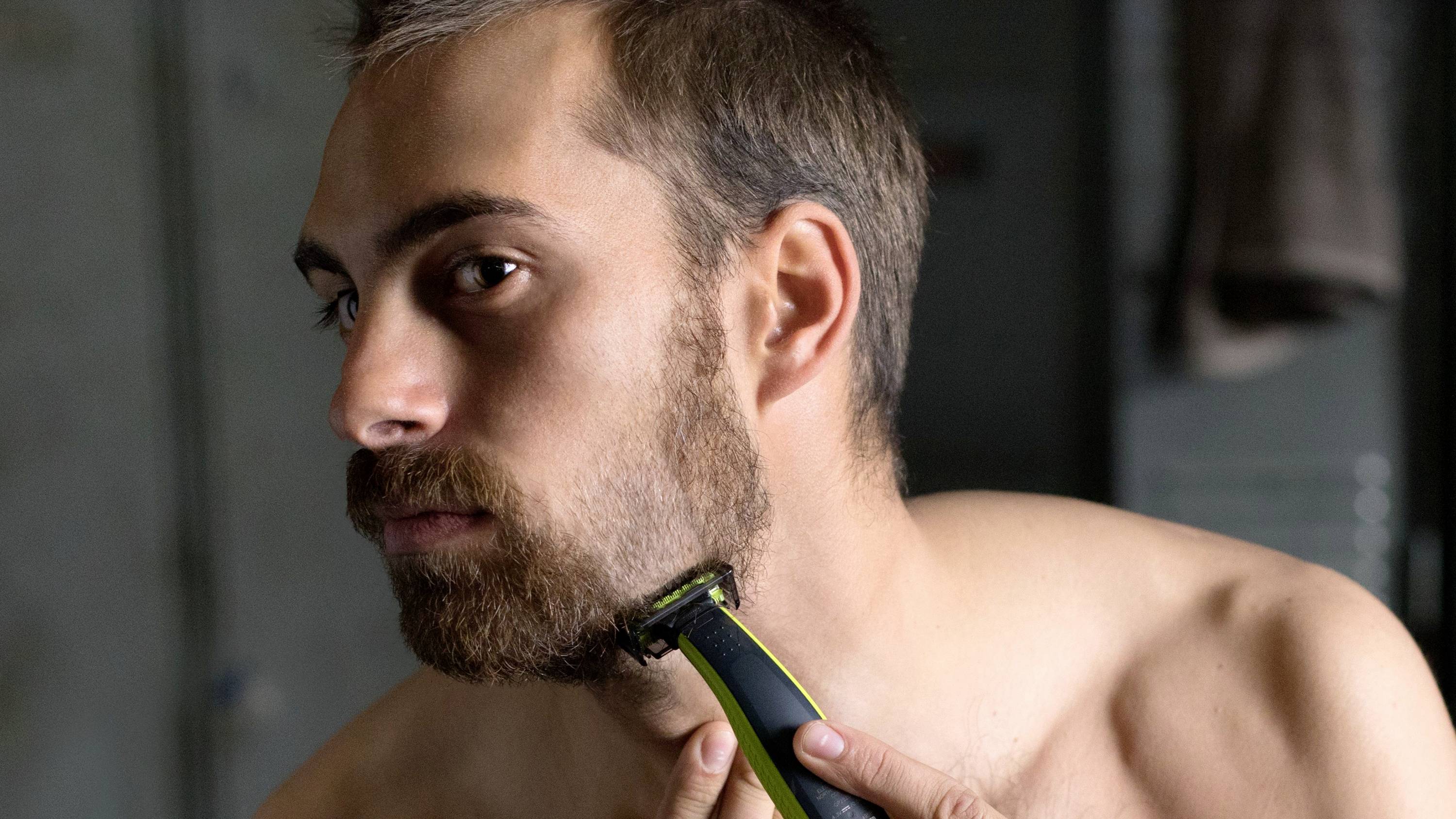 Un homme taille sa barbe avec un rasoir électrique dans une salle de bain.