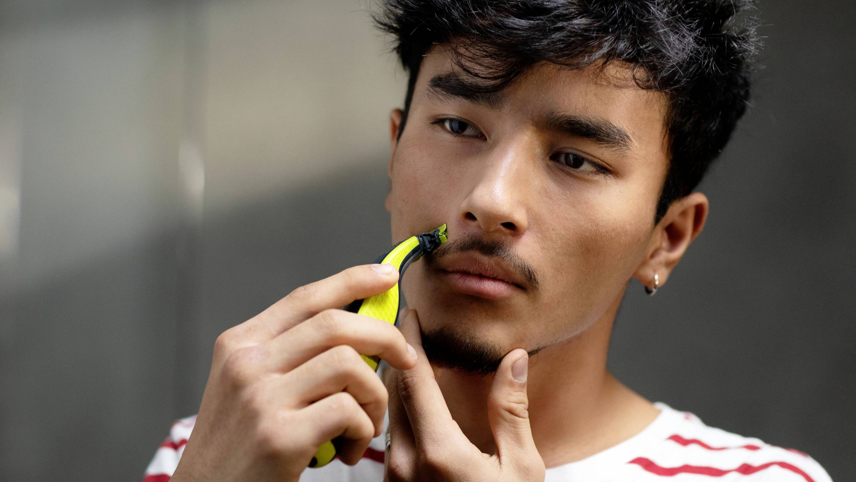 Un homme à barbe taille sa moustache avec un rasoir électrique dans une pièce bien éclairée.