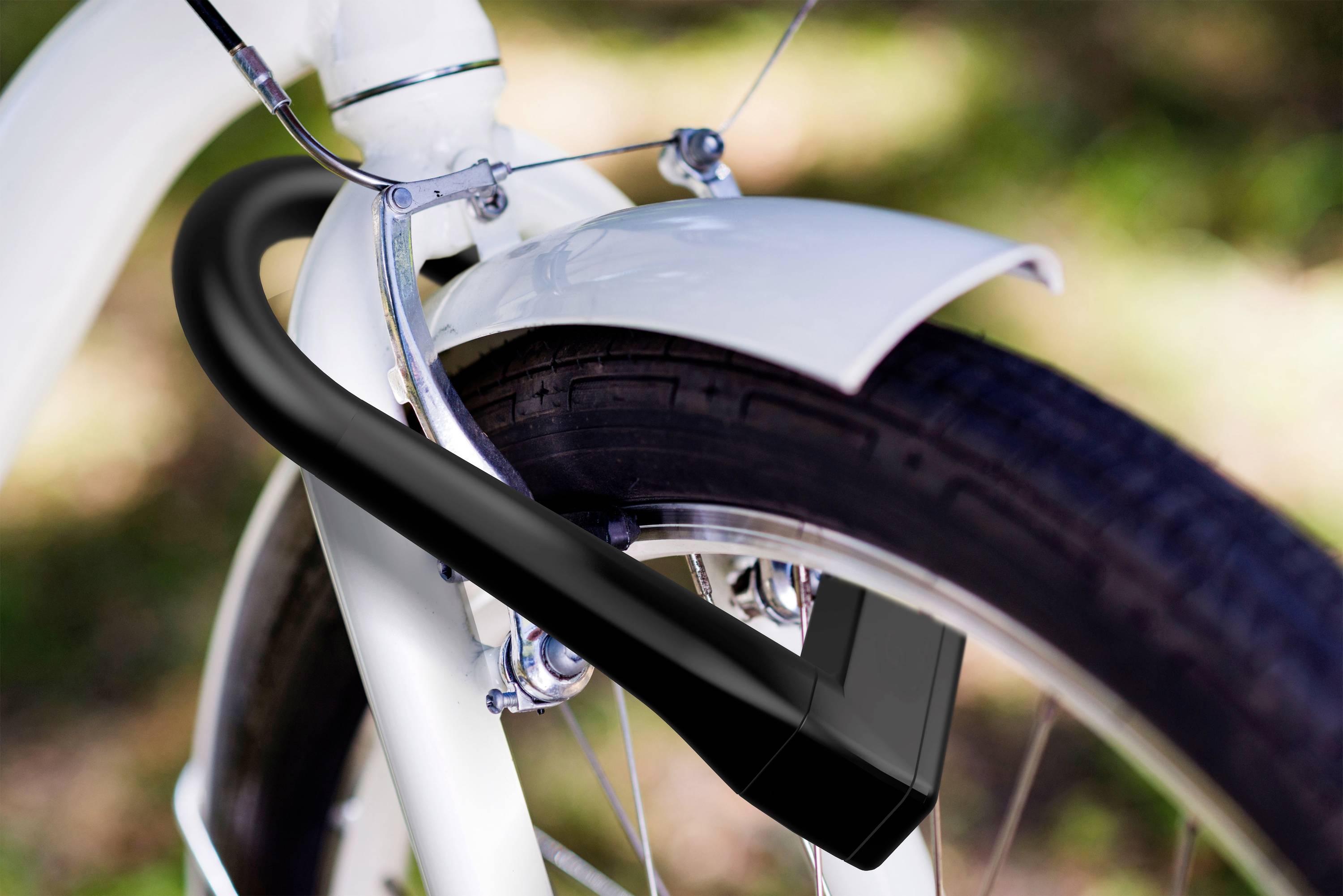 Un antivol noir sécurise la roue avant d'un vélo blanc. L'arrière-plan est flou et verdâtre.