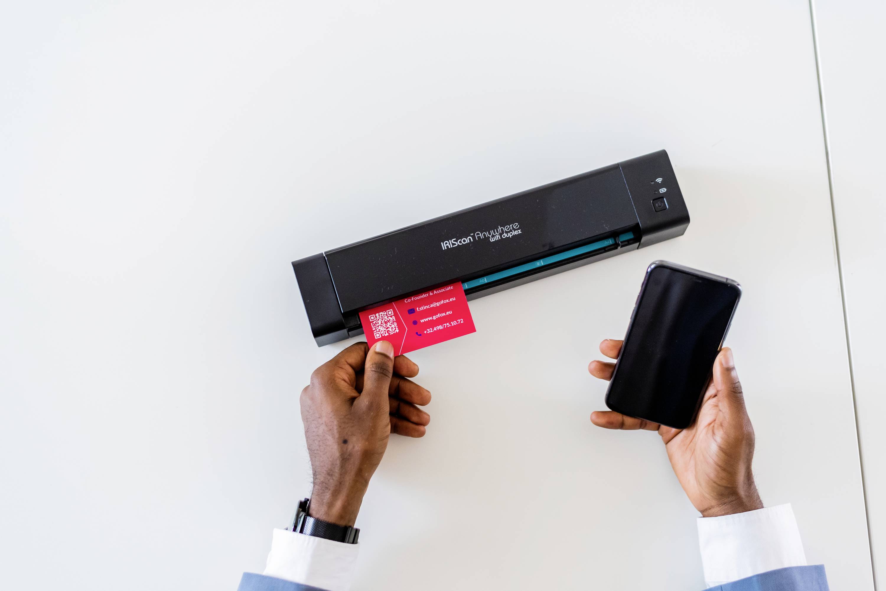 Une personne scanne une carte rouge avec un scanner portable. Dans l'autre main, elle tient un smartphone.
