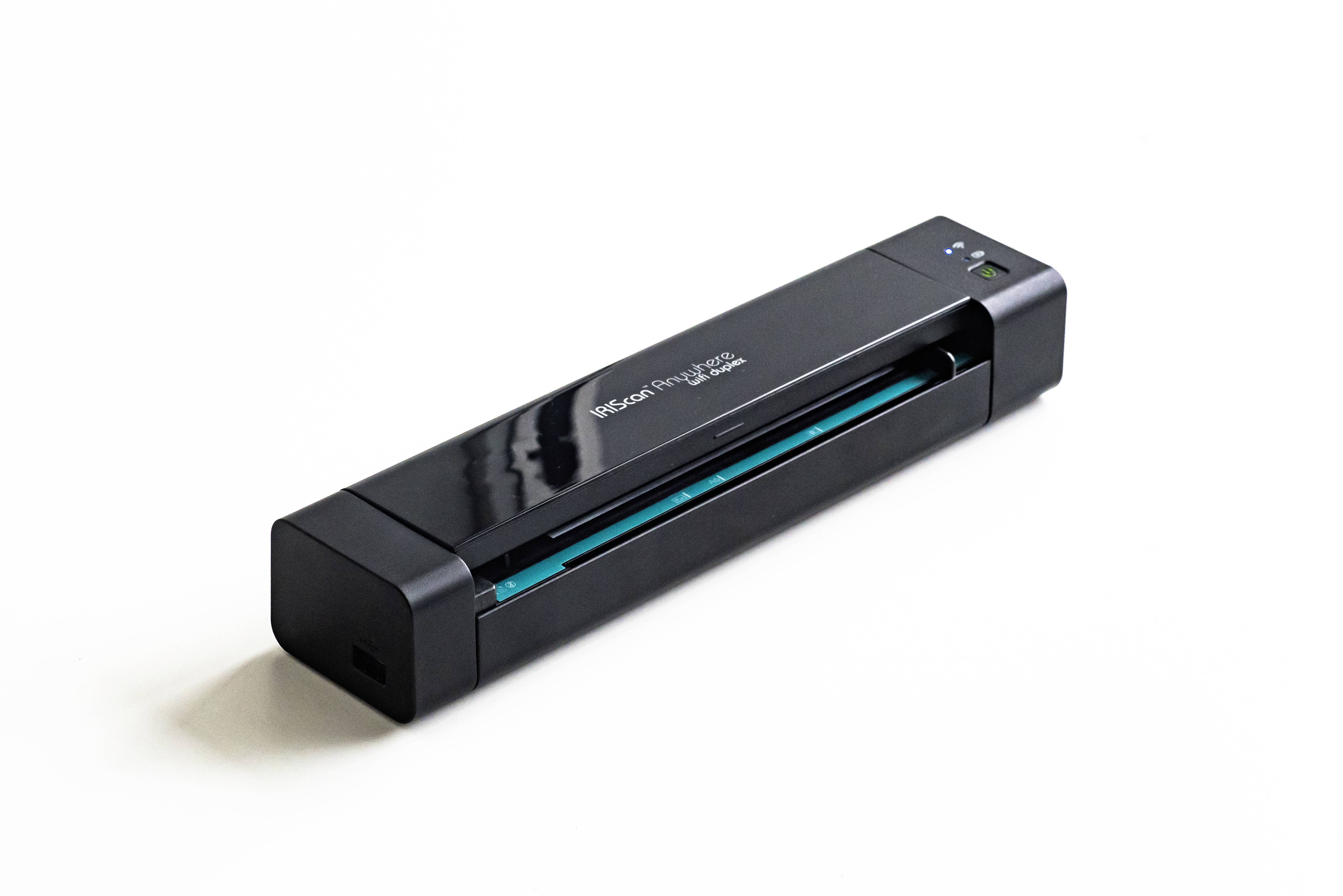 Un scanner de documents compact et noir sur un fond blanc. L'appareil est allumé et prêt à numériser des documents.