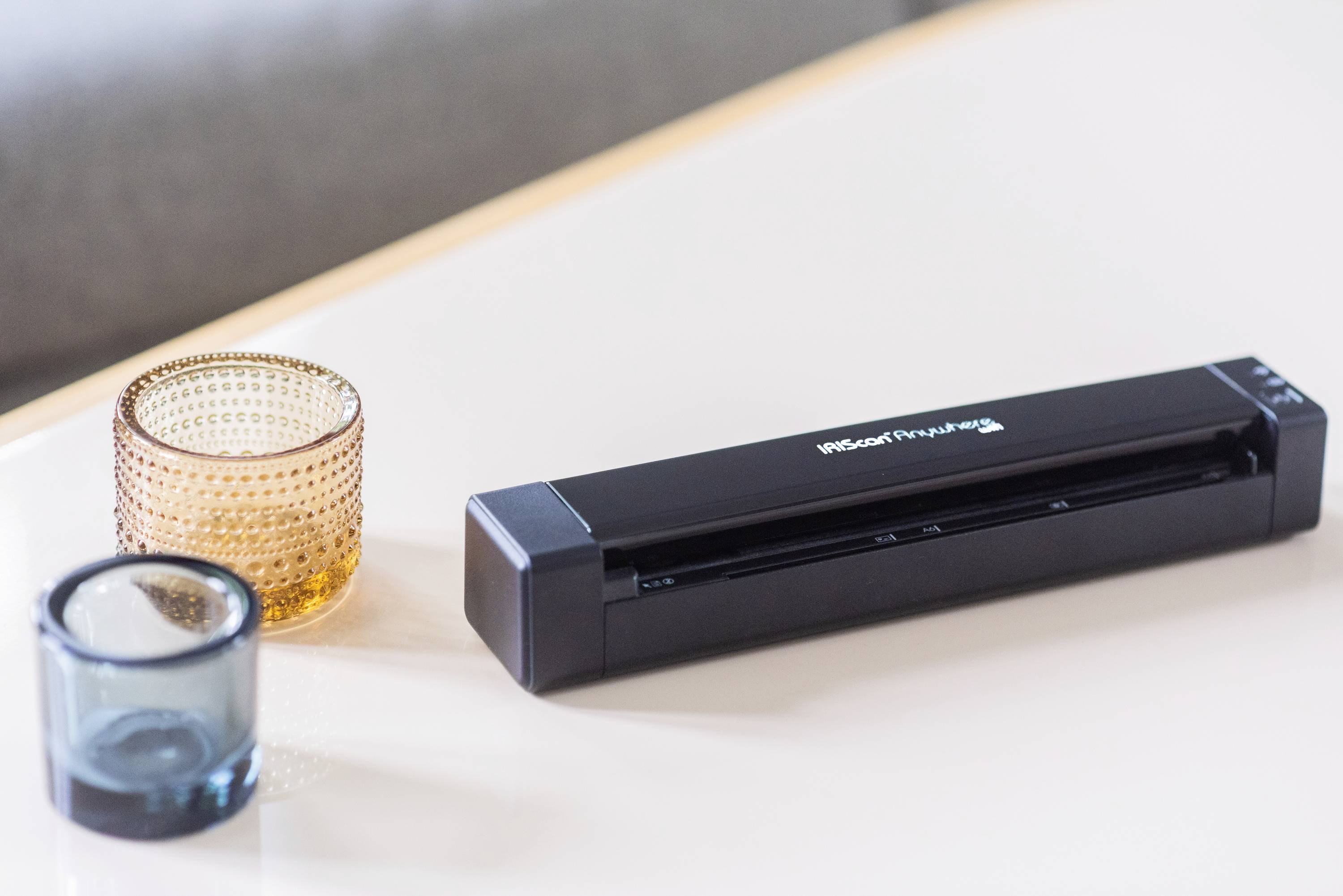 Un scanner portable est posé sur une table à côté d'un verre ambré et d'un verre bleu.
