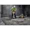 Une personne en tenue de protection utilise un marteau-piqueur pour briser du béton dans un environnement de chantier.