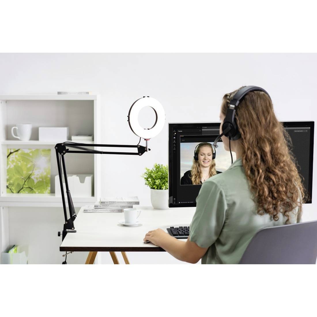 Une femme portant des écouteurs est assise à un bureau, regardant un écran et visible lors d'un appel vidéo.