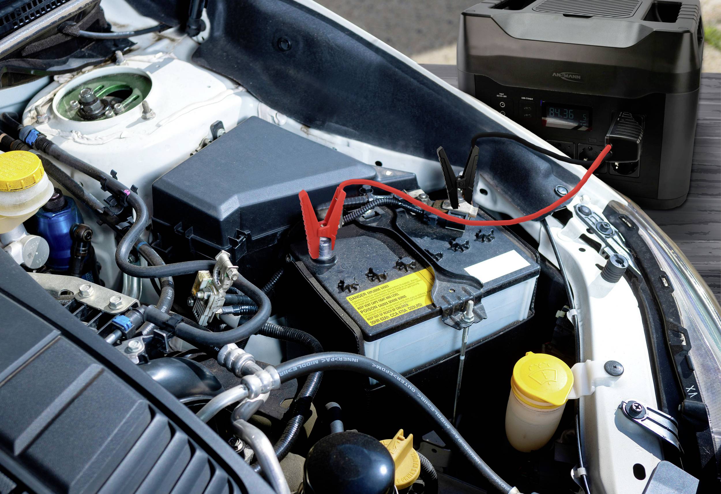 Une voiture démarre à l'aide d'une batterie de démarrage portable. Les câbles sont connectés à la batterie de la voiture pour lancer la charge.