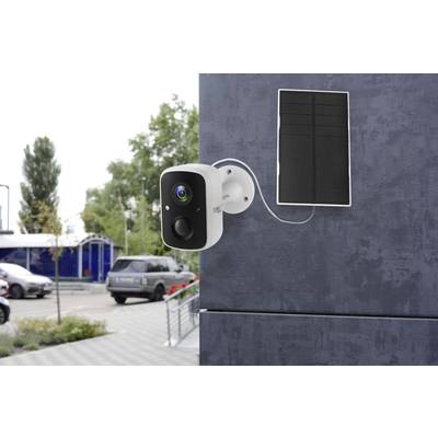 Caméra de surveillance fixée sur un mur, connectée à un module solaire. Des voitures et des bâtiments en arrière-plan suggèrent un parking.