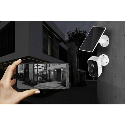 Une personne tient un smartphone affichant des images en direct provenant d'une caméra de surveillance. La caméra est installée sur une maison.