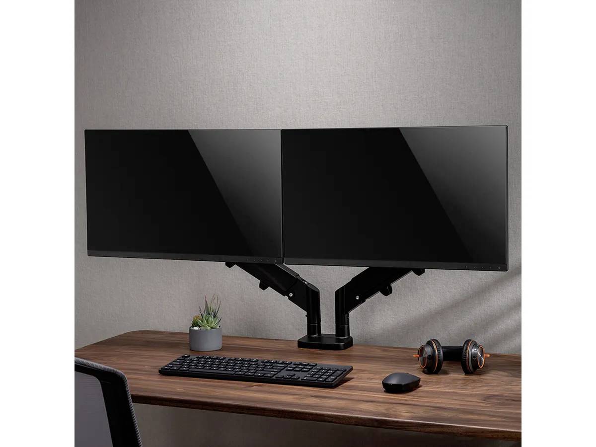 Support de moniteur double maintenant deux écrans au-dessus d'une table en bois avec clavier, souris, casque et plante.