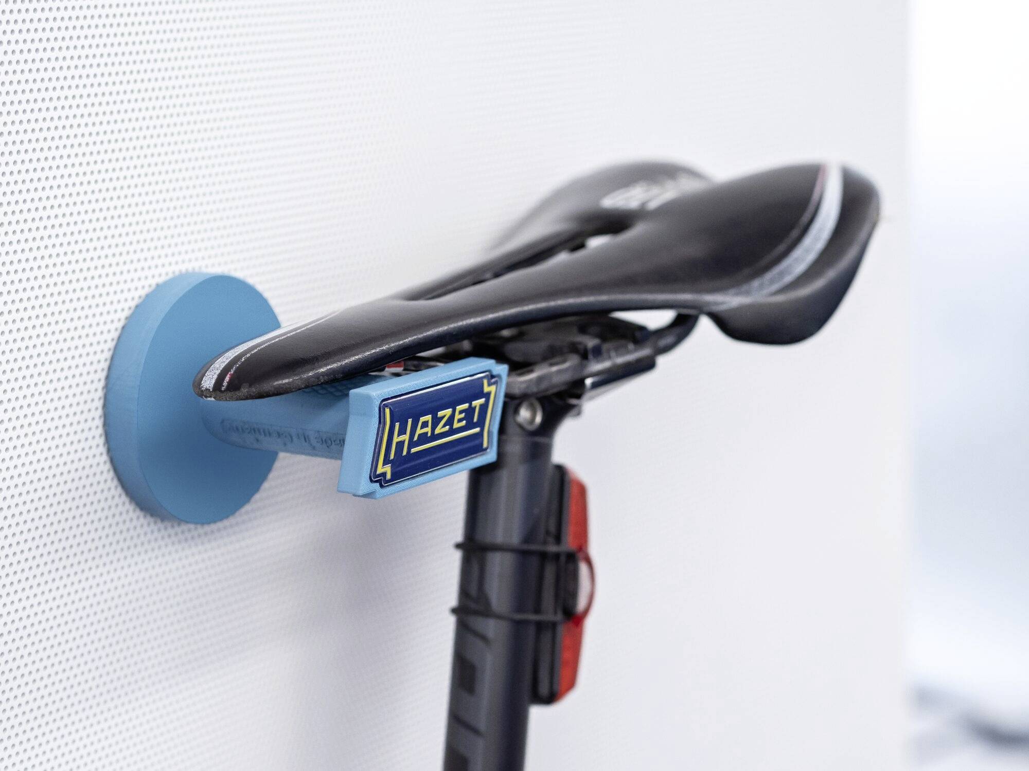 Un vélo est fixé par sa selle à un support mural. Le support est bleu, la selle est noire et le vélo est en position verticale.
