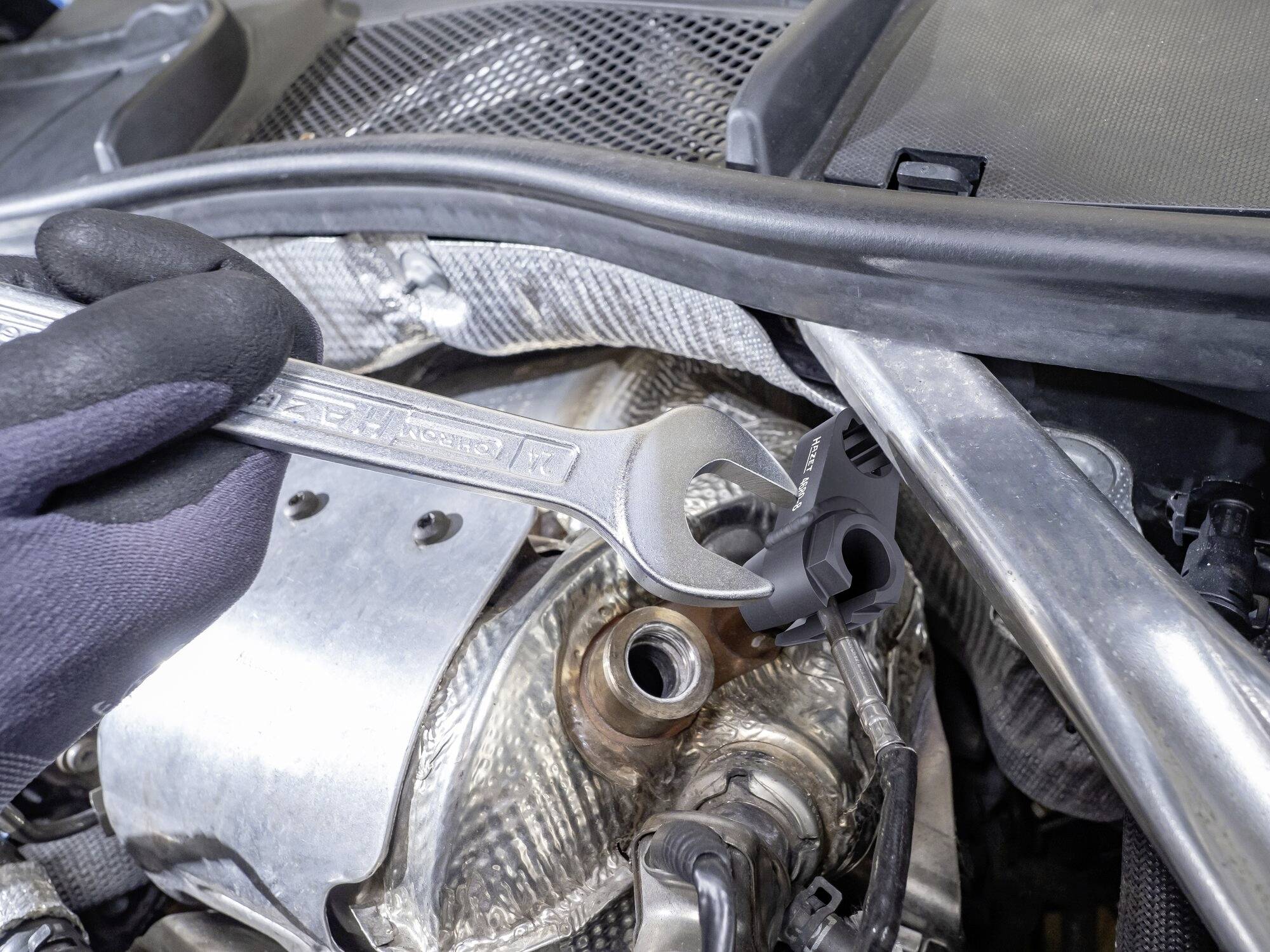 Un mécanicien tient une clé à molette dans le compartiment moteur d'une voiture. La clé à molette saisit un écrou sur une pièce complexe.