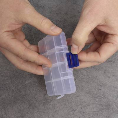Des mains ouvrent un boîtier transparent en plastique avec un rabat de fermeture bleu.