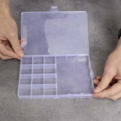 Une boîte en plastique transparente et ouverte à plusieurs compartiments est tenue par deux mains, une à gauche et une à droite.