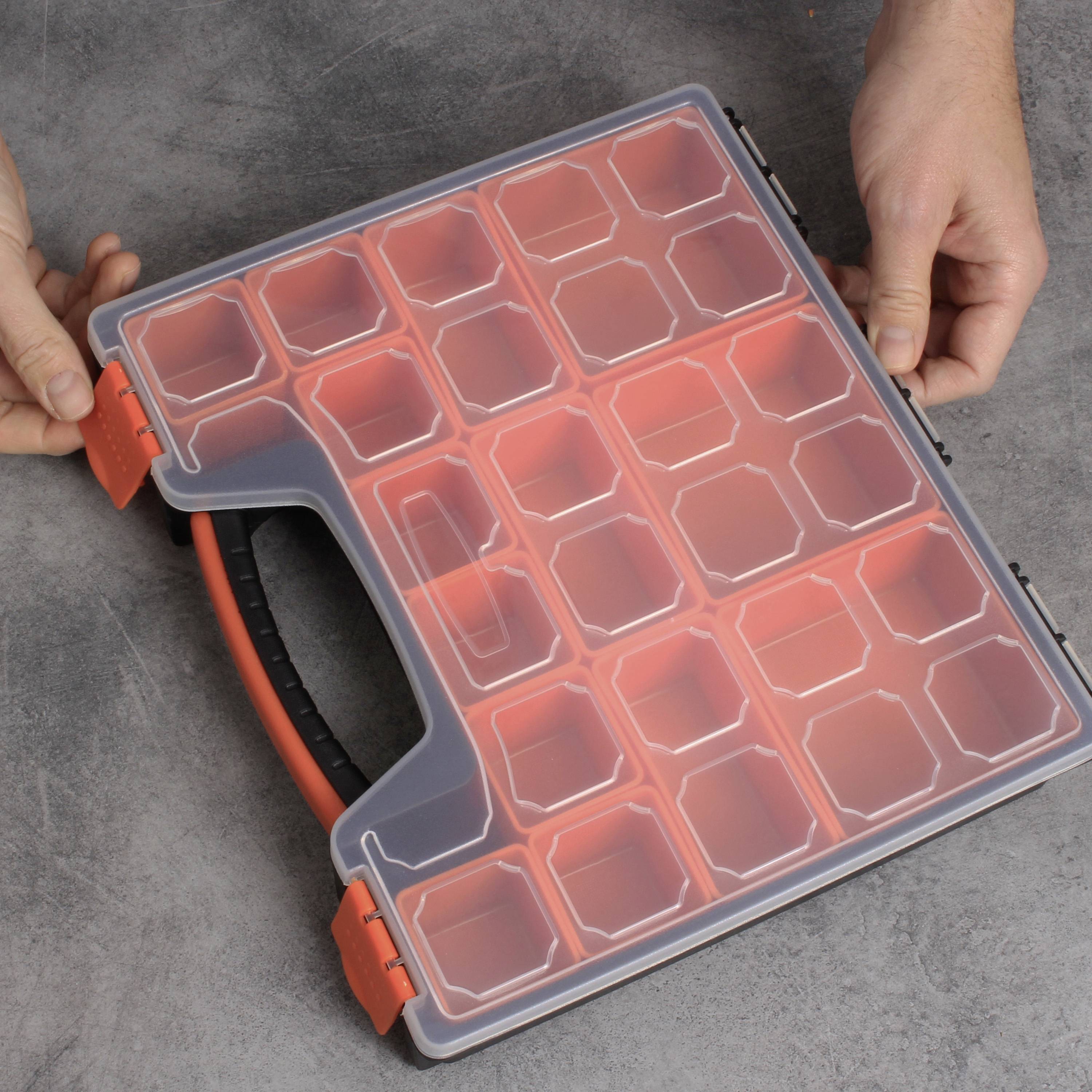 Une personne tient un organiseur en plastique transparent avec des compartiments rouges sur un fond gris.