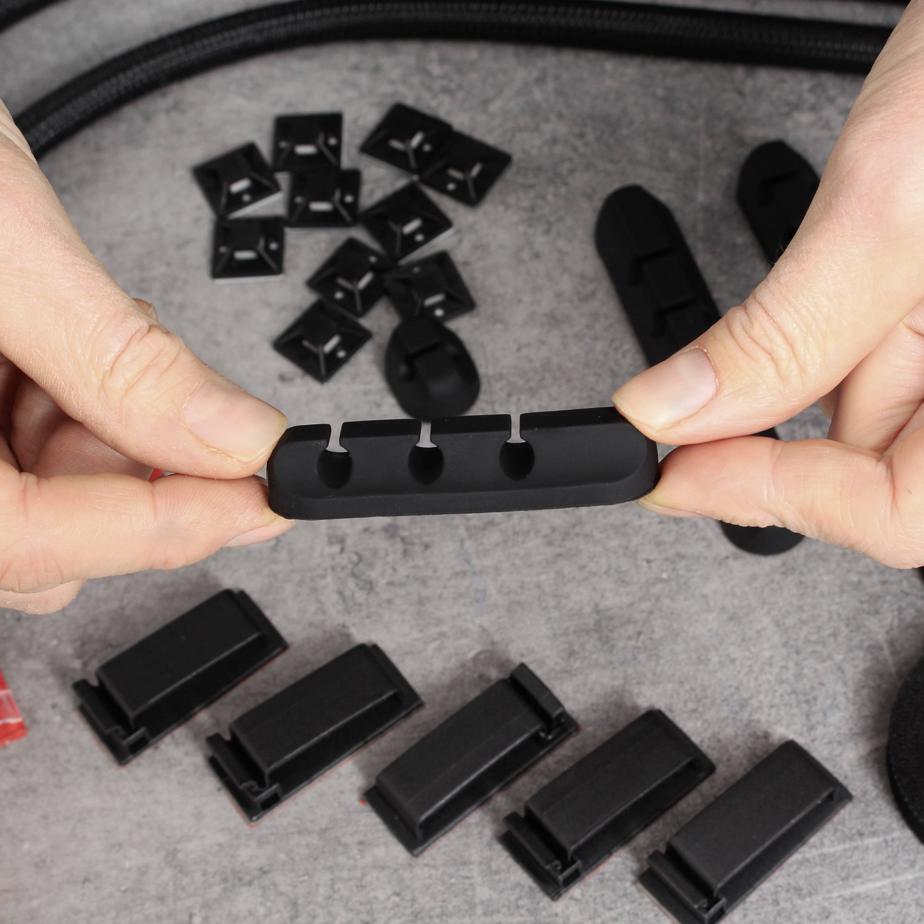 Deux mains tiennent une pièce en plastique noir rectangulaire avec trois ouvertures rondes, flanquée de pièces similaires sur une table.