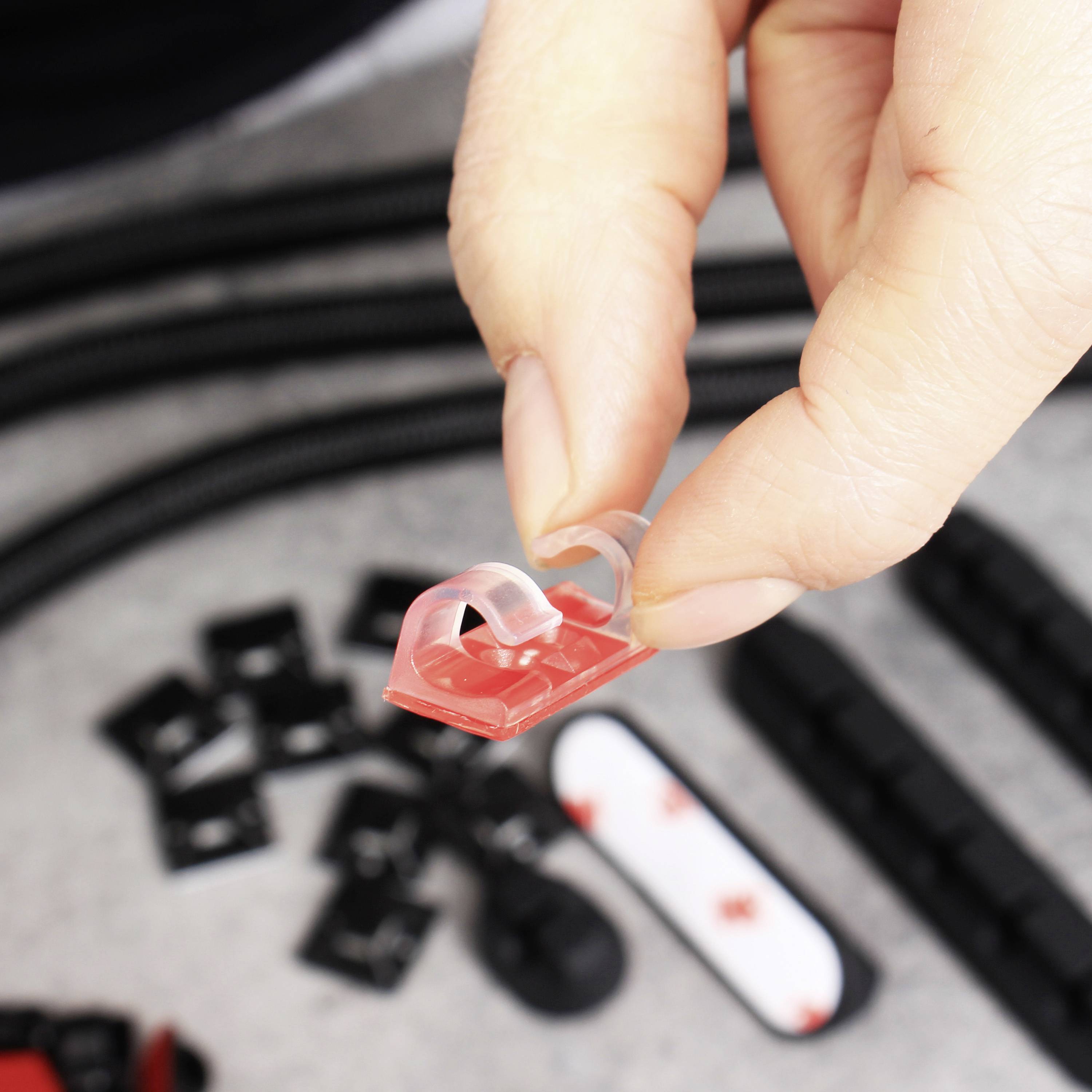 L'illustration montre une main tenant un morceau de plastique rouge avec une surface adhésive transparente. D'autres petites pièces sont visibles en arrière-plan.