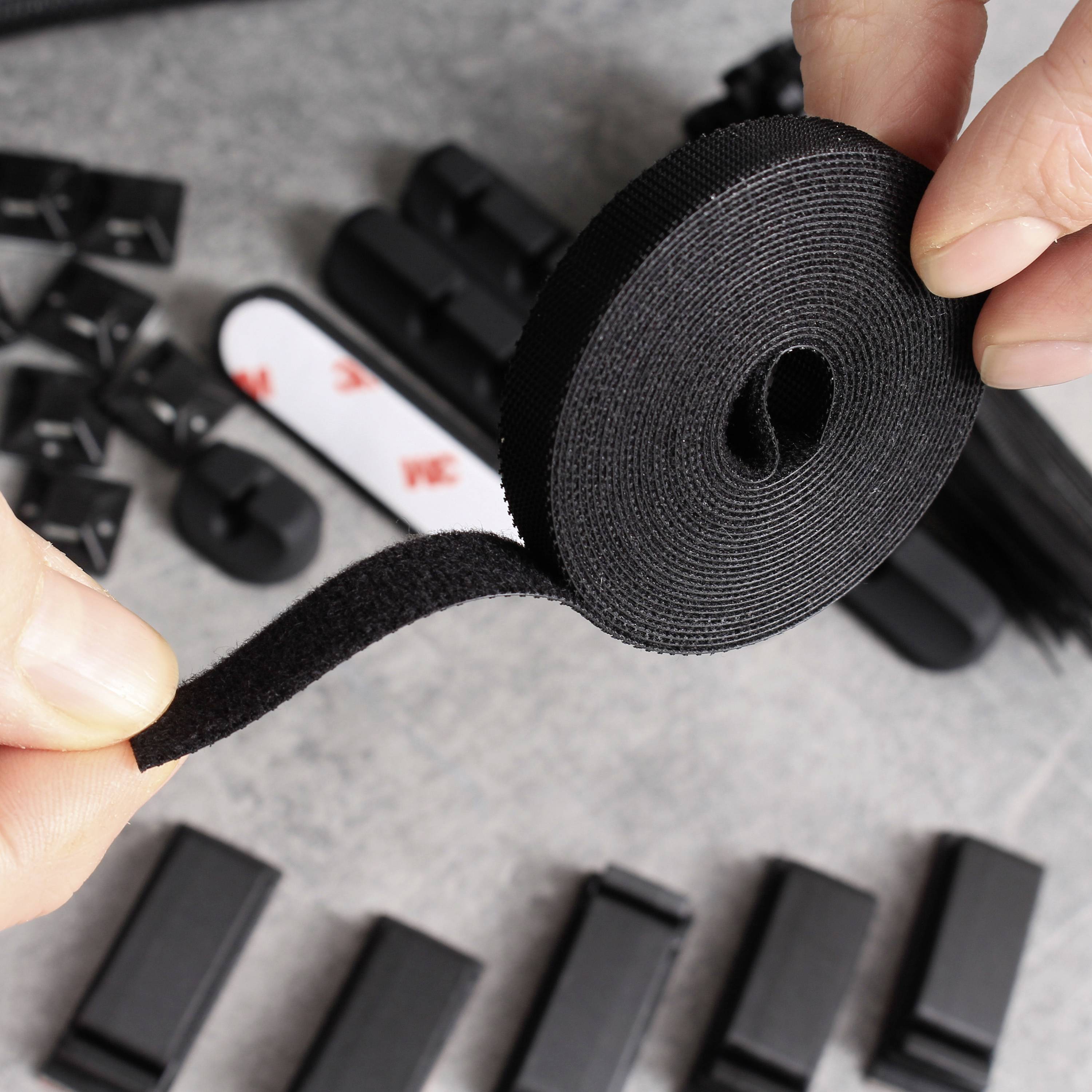 Une main tient une fermeture autoagrippante noire, et plusieurs clips de fixation noirs sont posés en arrière-plan sur une surface grise.