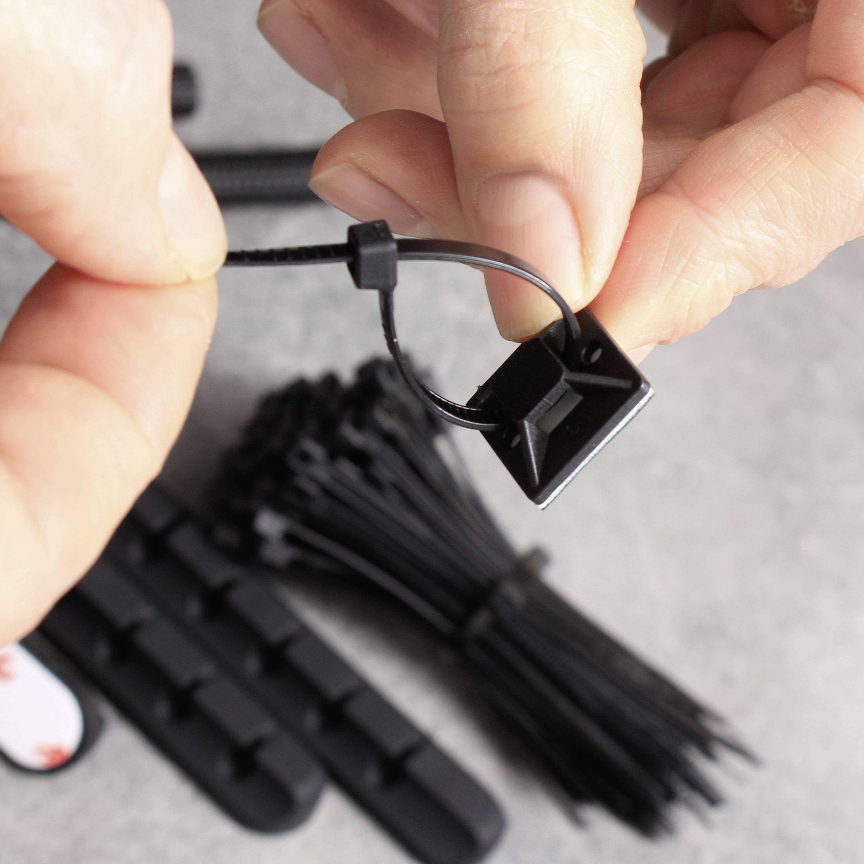 Une personne tient un ensemble de supports de câbles avec des attaches. L'accent est mis sur la fixation d'un serre-câble dans un petit clip en plastique.